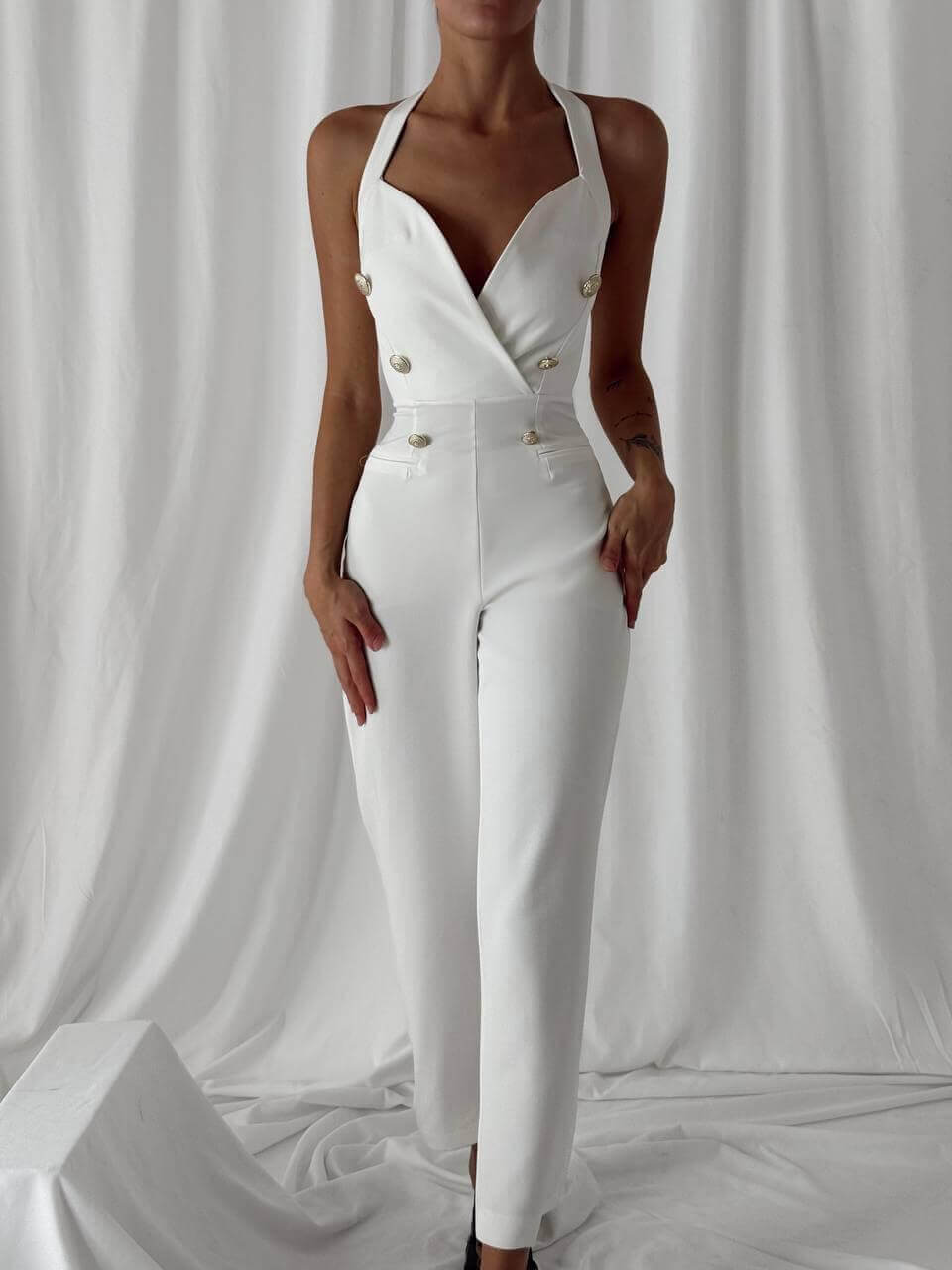 Elegant white women's overall with a deep V-neck and decorative buttons, perfect for stylish outfits and events.