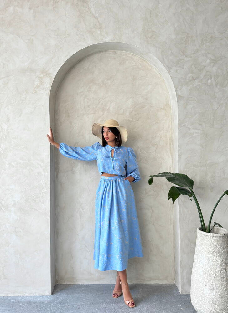Model in a blue Boho print linen two-piece set posing in an archway with a potted plant.