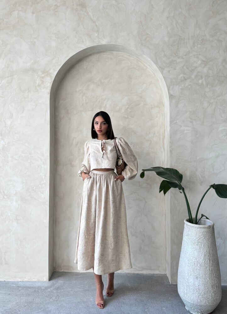 Model in boho print linen two-piece set featuring a chic blouse and matching skirt against a textured wall.