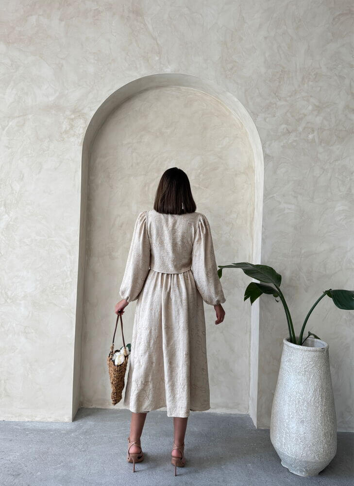Back view of a woman in a boho print linen two-piece set, styled with a woven bag and set against a textured wall.