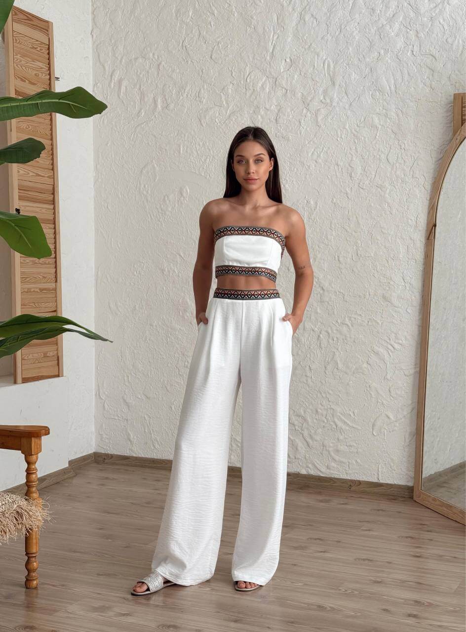 Woman wearing a white bohemian two-piece set with embroidered crop top and wide-leg pants, standing in a natural setting.