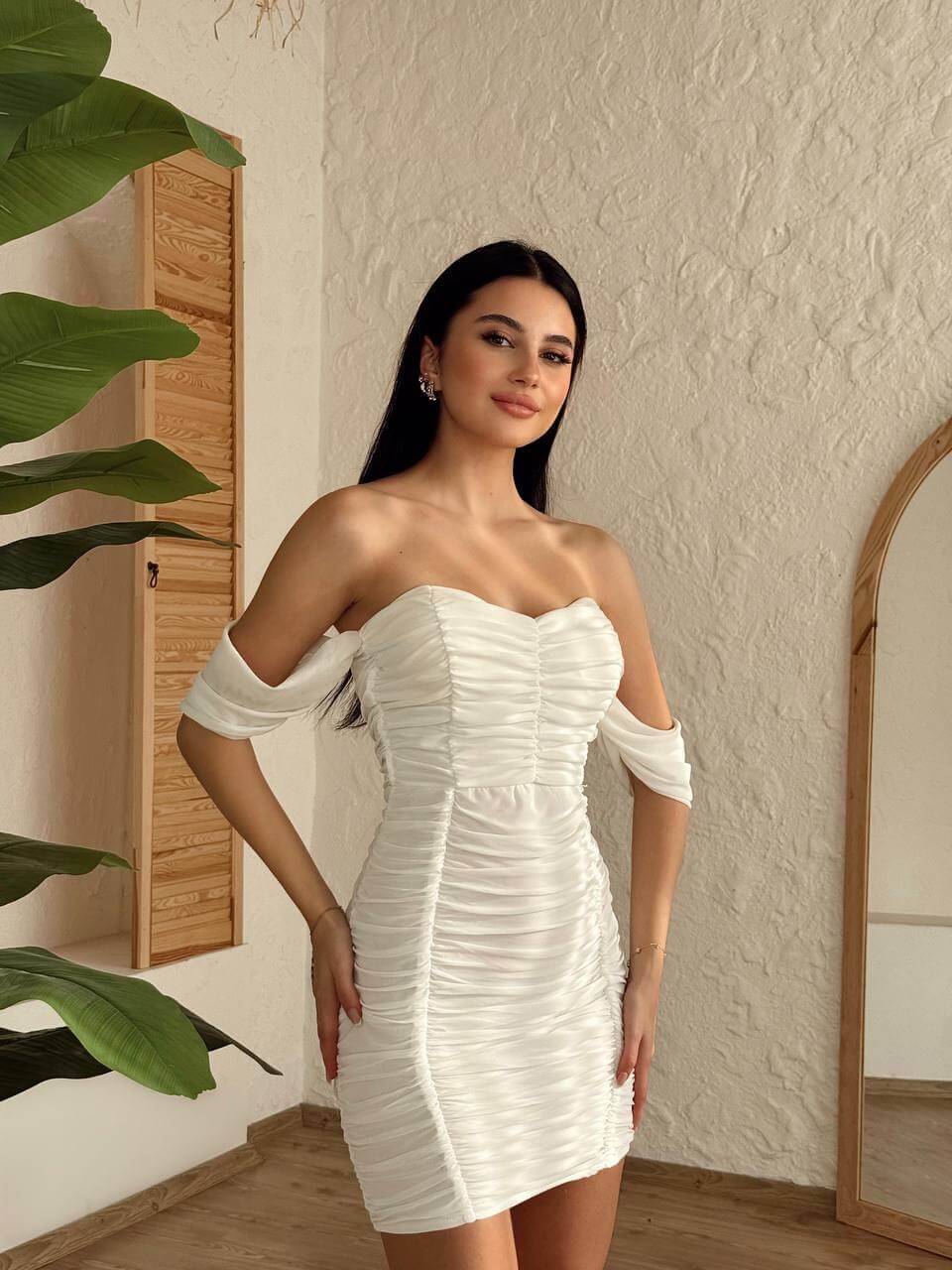 A white off-shoulder ruched mini dress displayed on a mannequin, highlighting the dress's full length and form