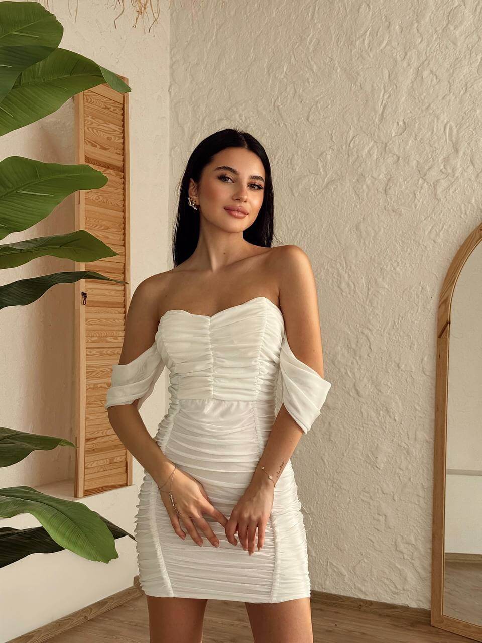 A model wearing a white off-shoulder ruched mini dress, styled with elegant accessories for a summer party look.