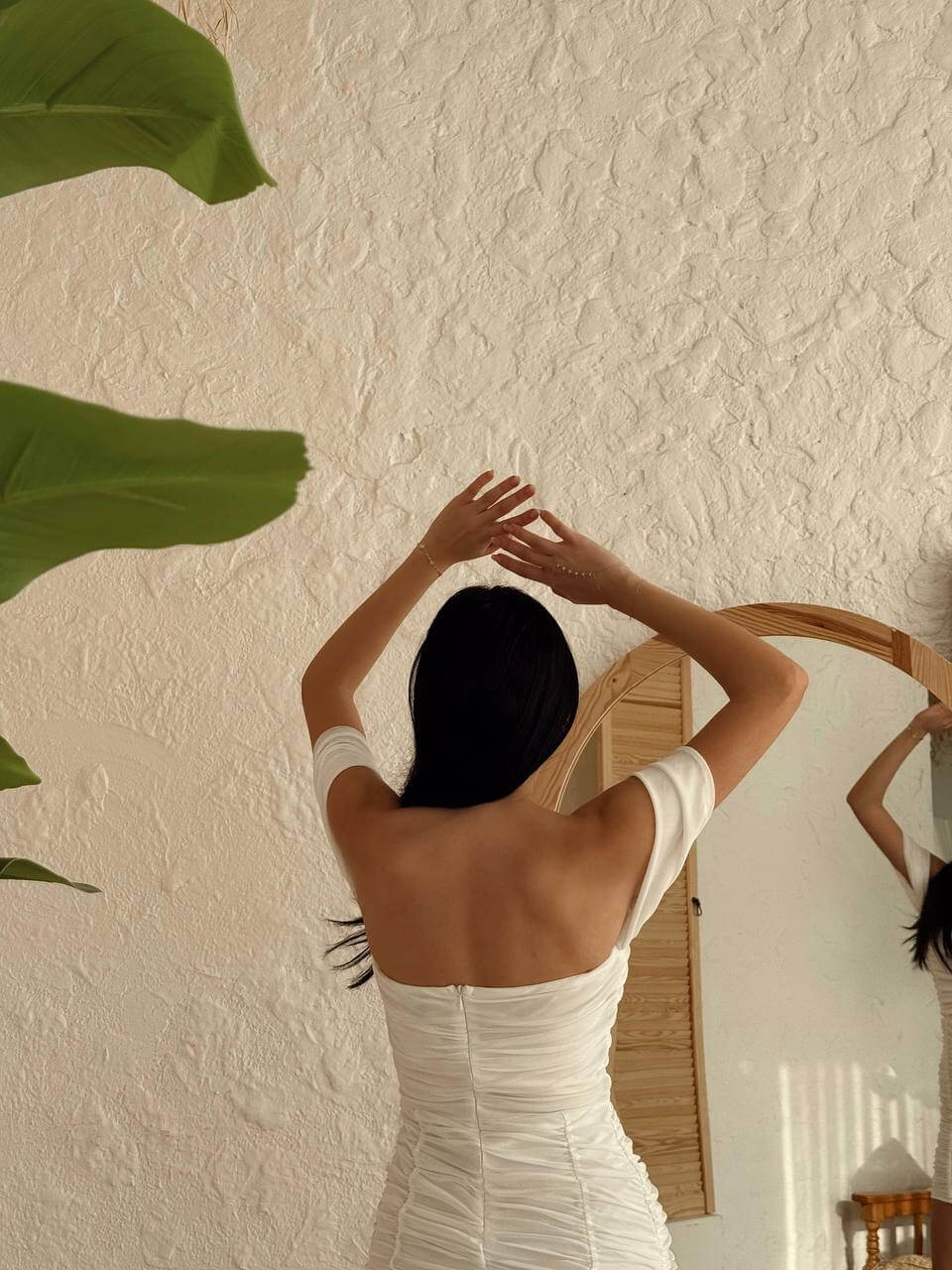 Back view of a woman wearing a white off-shoulder ruched mini dress, emphasizing the dress's silhouette and ruching details.