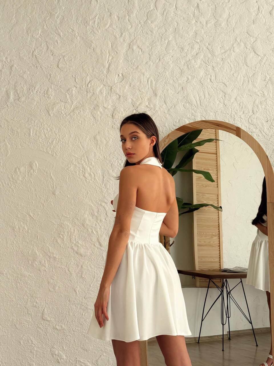 Short white-colored dress with a halter neckline, open back, and flared skirt.