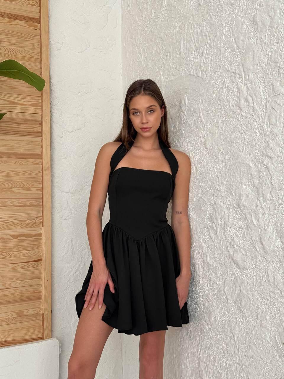 Short black-colored dress with a halter neckline, open back, and flared skirt.