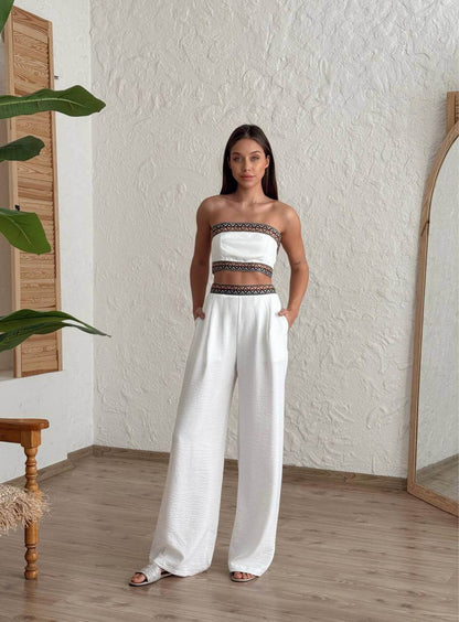Woman wearing a white bohemian two-piece set with embroidered crop top and wide-leg pants, standing in a natural setting.